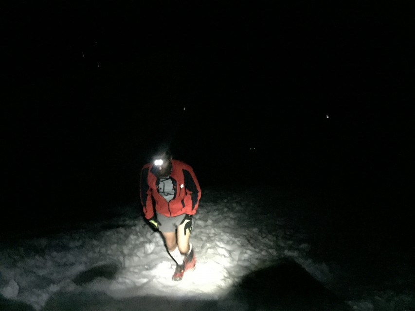 Runner reaches the summit late at night. Headlamps shine below. 